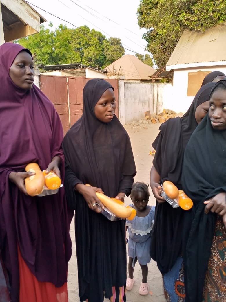 Women in black abayas receive bread and fruit at a food distribution